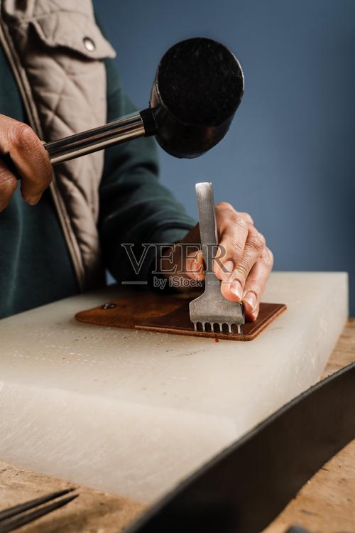 工匠正在使用线条冲孔机和锤子冲孔真皮以创造天然皮革制品工匠制作